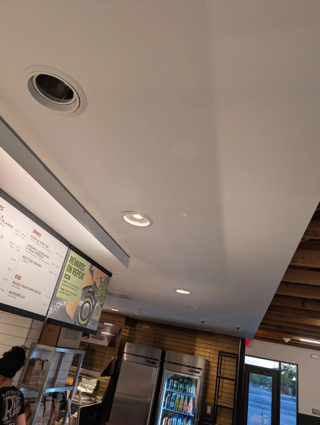 Cafe interior with ceiling lights, menu boards, and a counter near a glass door