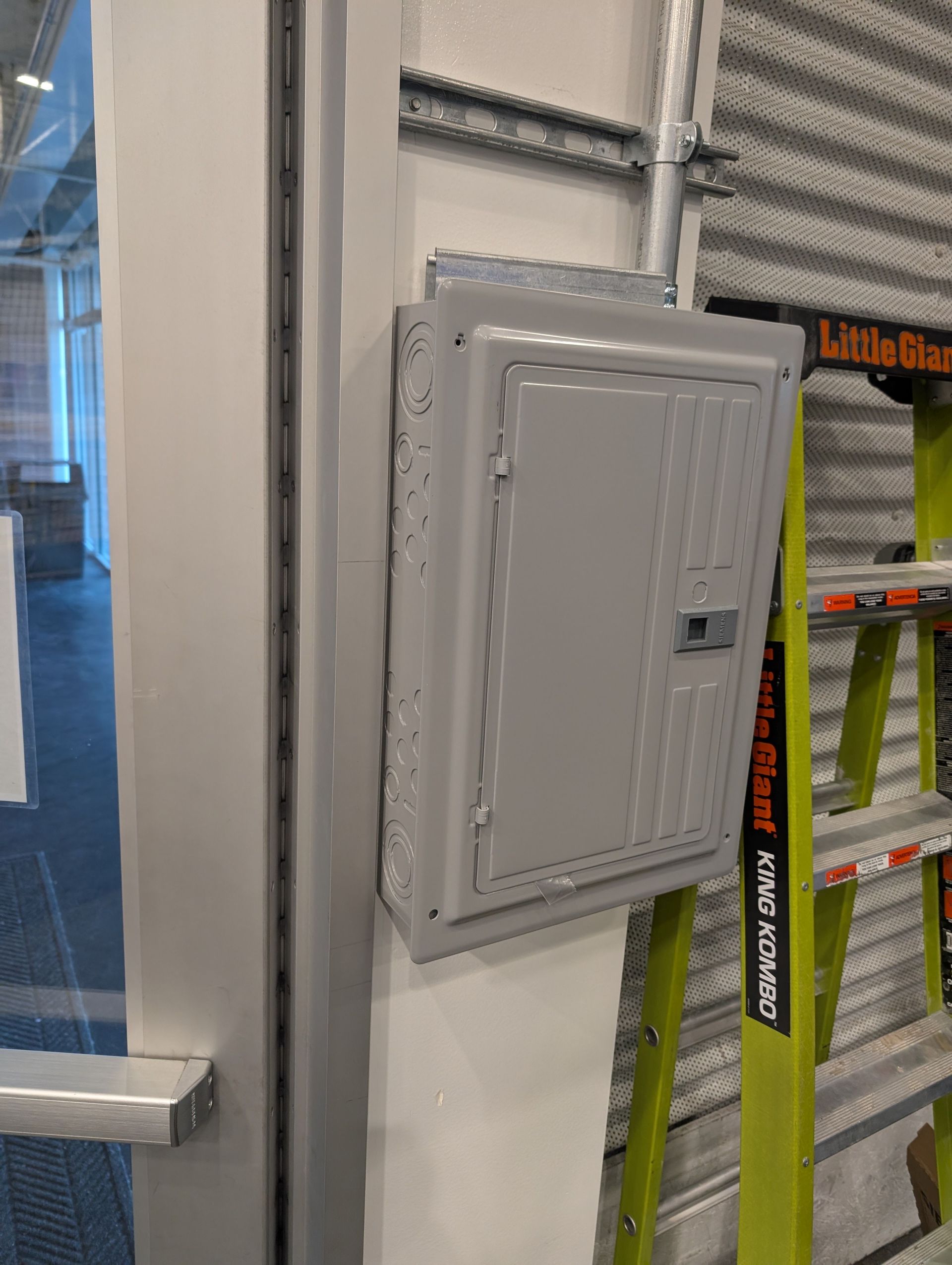 Gray electrical panel mounted on a white wall beside metal shelving and store signage.