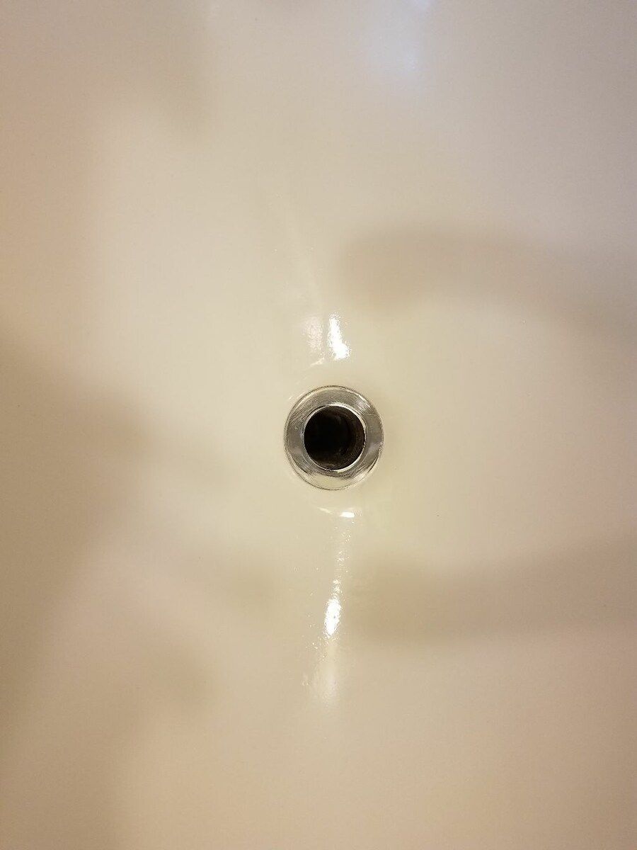 A close up of a drain hole in a bathroom sink.
