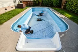 Two people on a vinyl liner in an empty above-ground swimming pool in a backyard