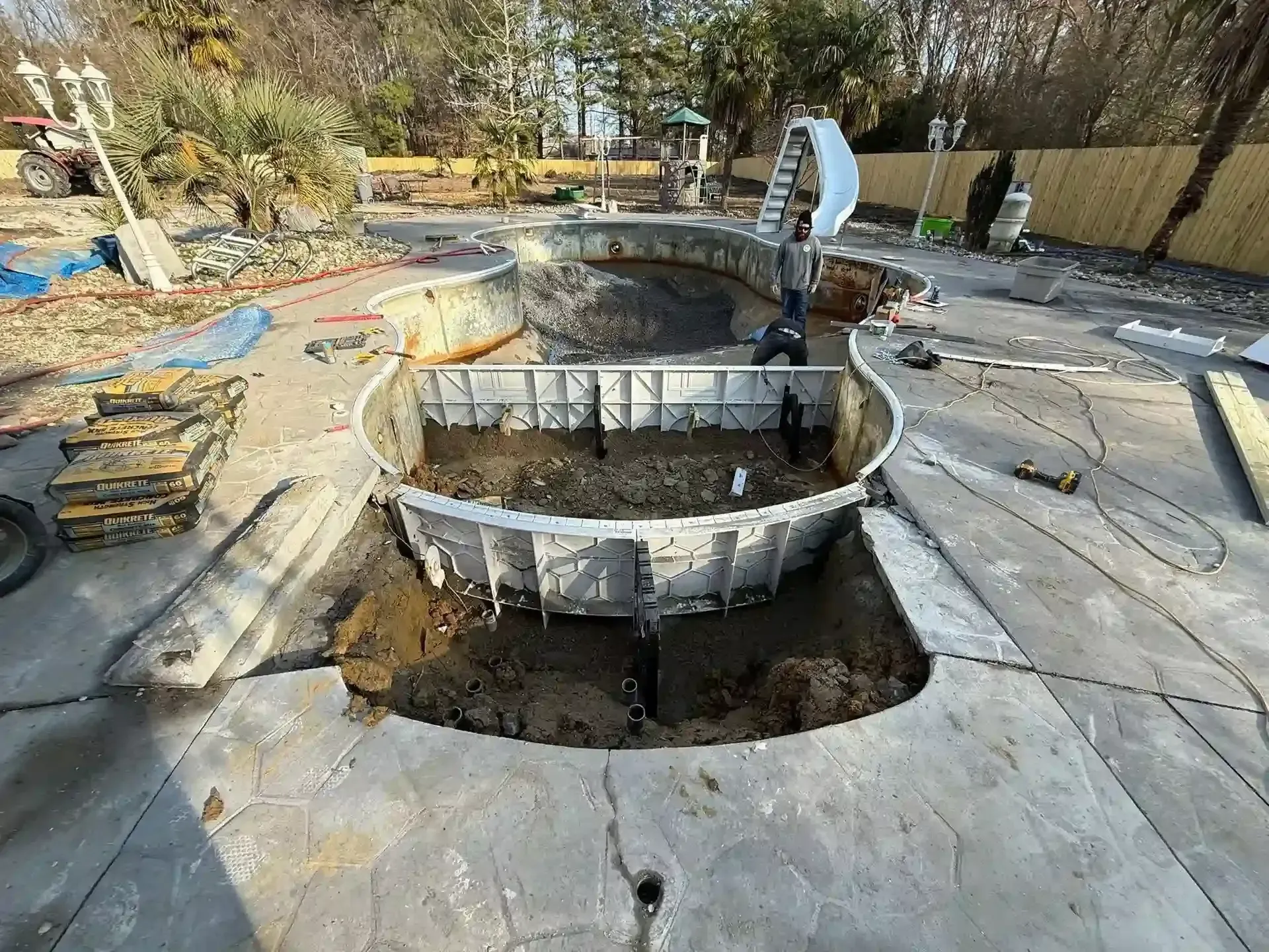 Backyard under construction with a large dug-out pool or pond, concrete forms, and scattered tools