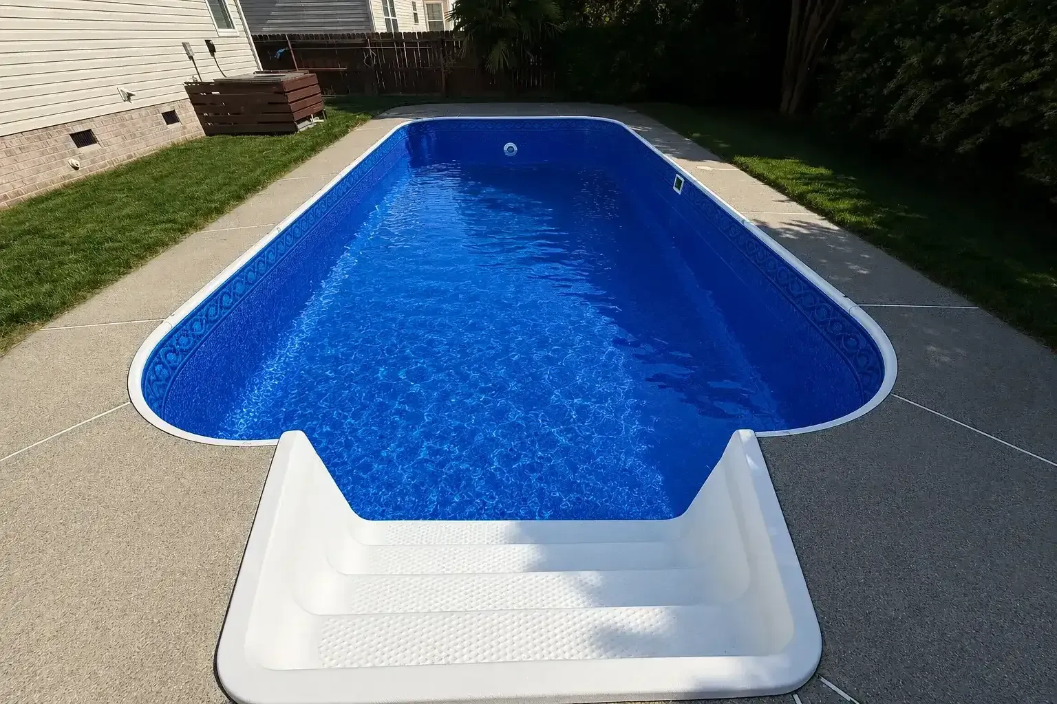 Backyard swimming pool with white steps and blue water on a concrete patio