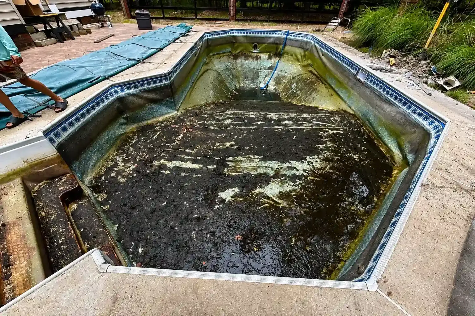 Large hexagonal concrete pond with murky water, surrounded by a paved walkway and blue tarp covering nearby ground.