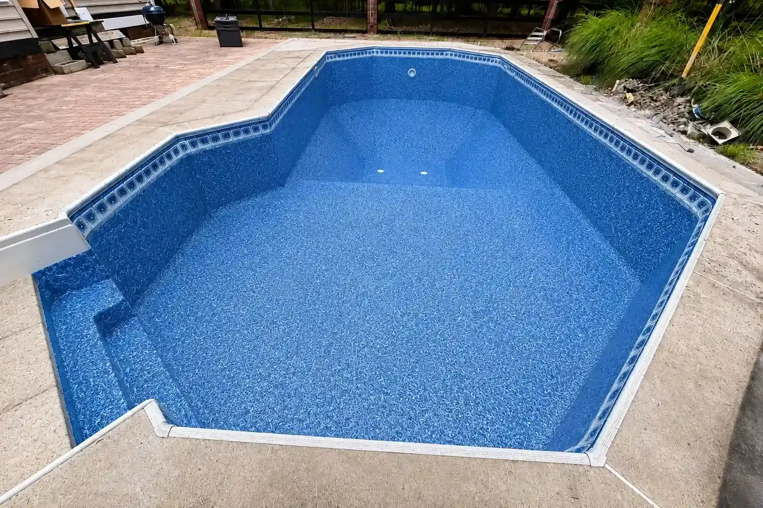 Empty blue swimming pool with a light stone deck outdoors