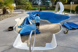 Empty drained pool covered with blue tarp, with a person standing inside near a metal ladder