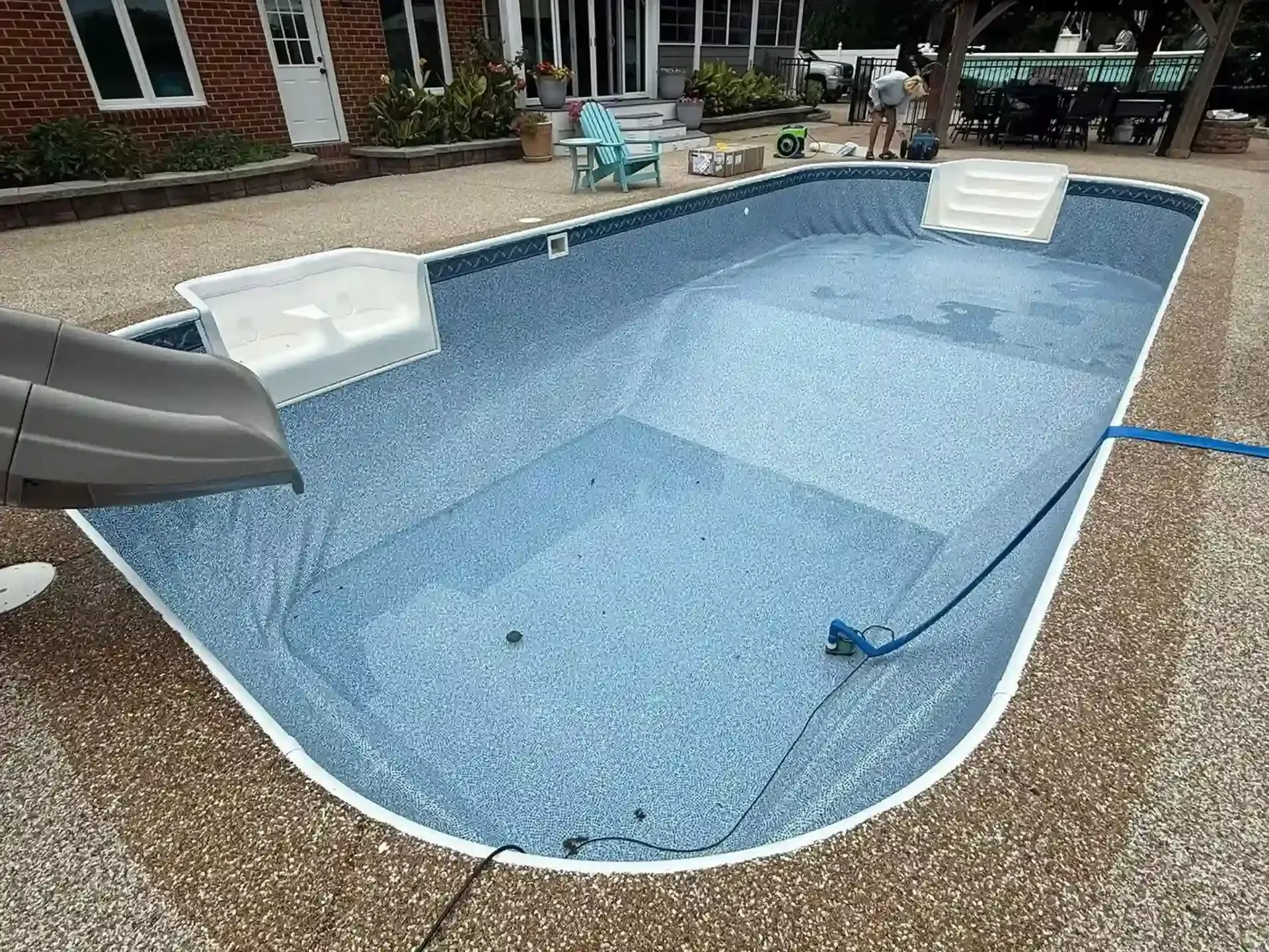 Small backyard swimming pool with blue water, a slide, and white poolside seating on a patio.