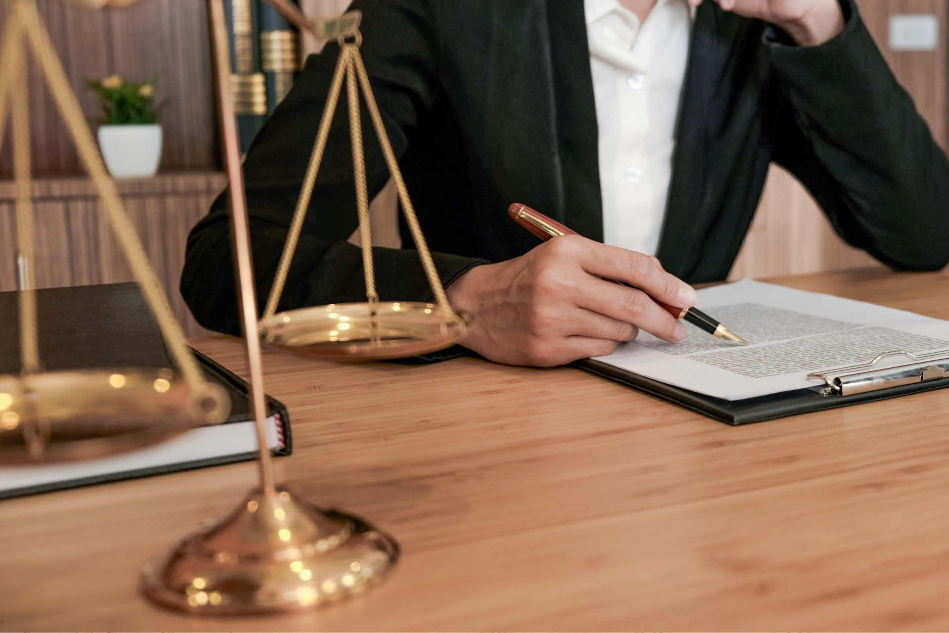 Lawyer writing notes at a desk with brass scales of justice in the foreground