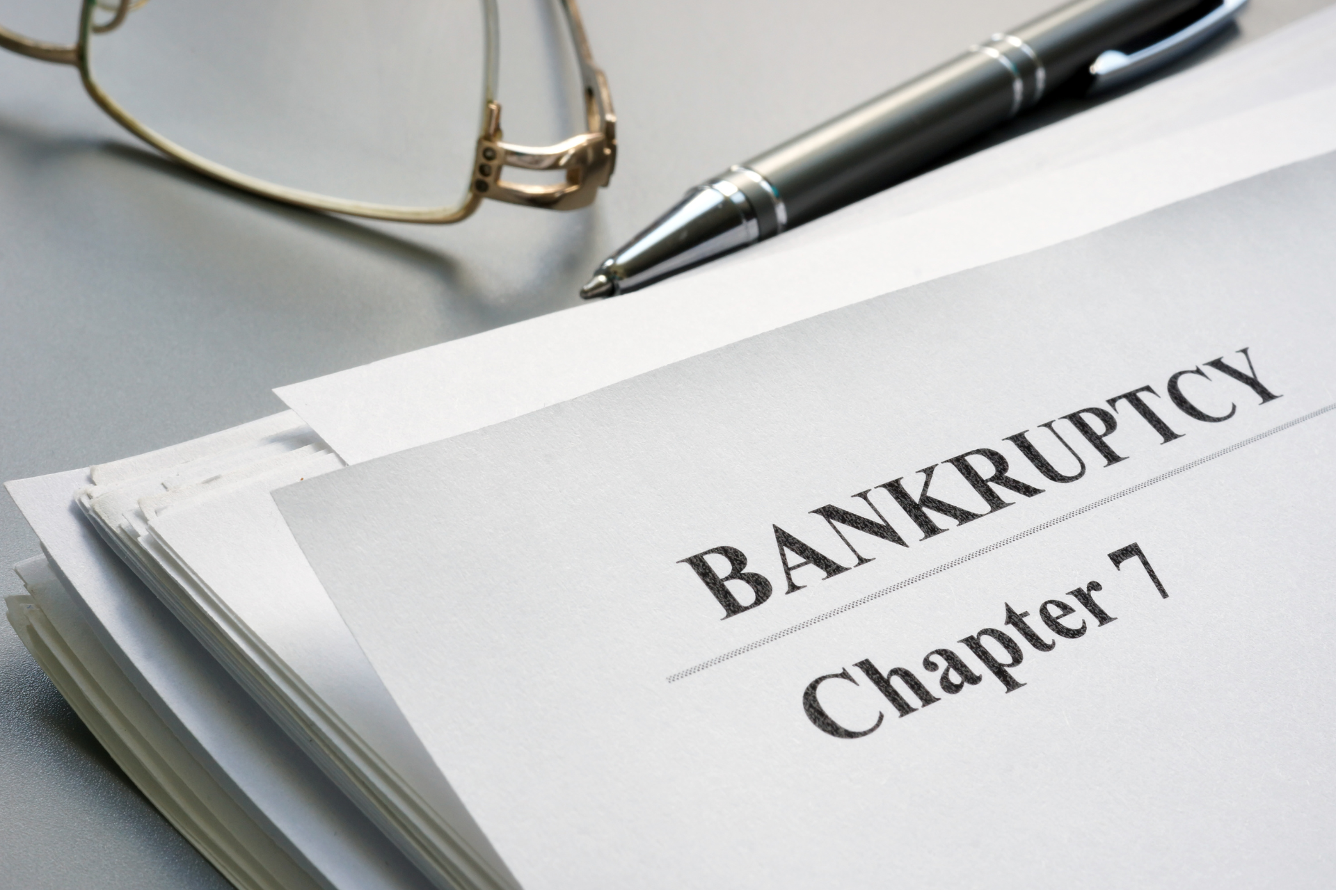 Documents labeled “BANKRUPTCY Chapter 7” beside eyeglasses and a pen