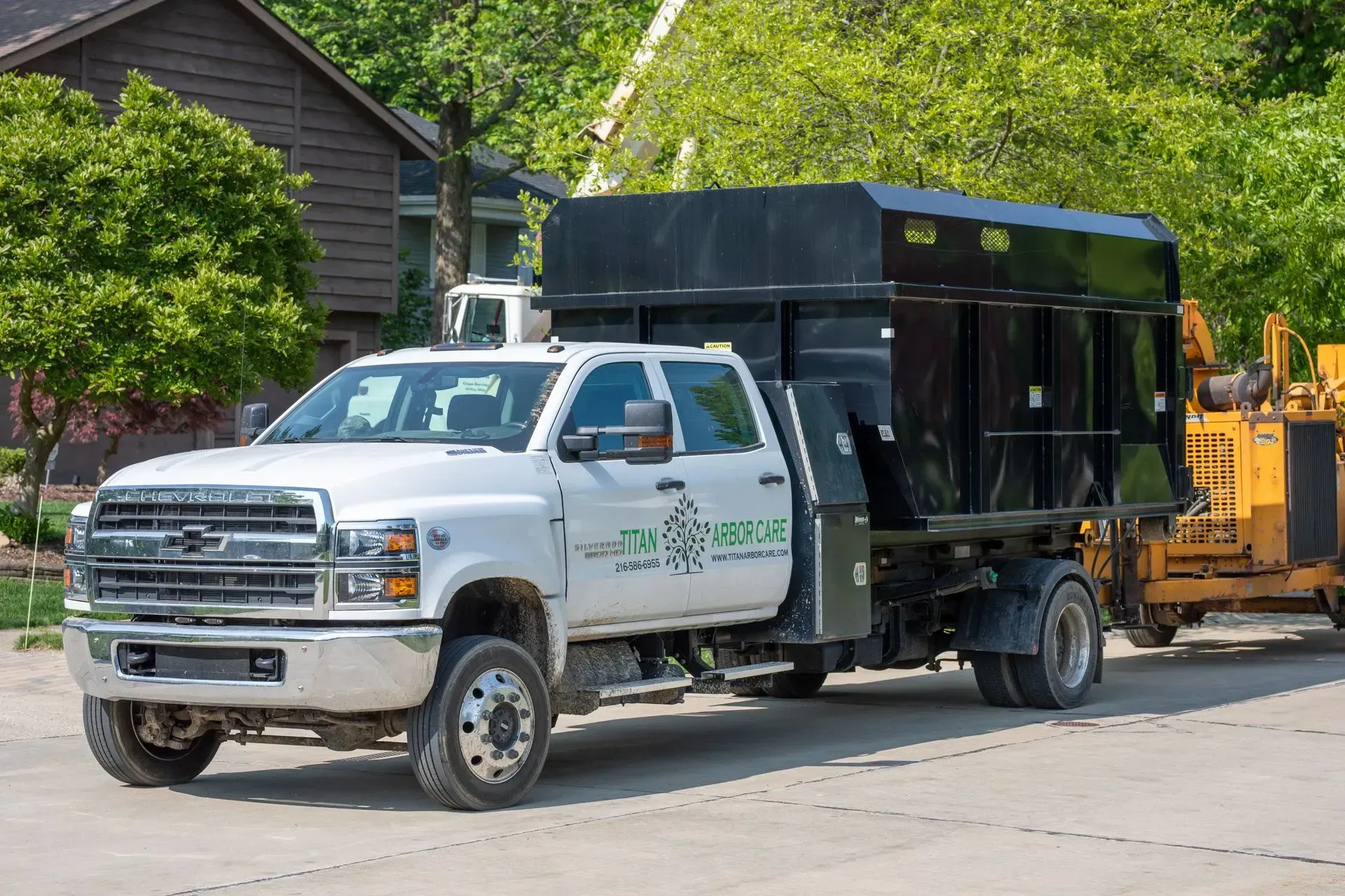 White Chevrolet truck with black dump bed, parked next to a yellow wood chipper.