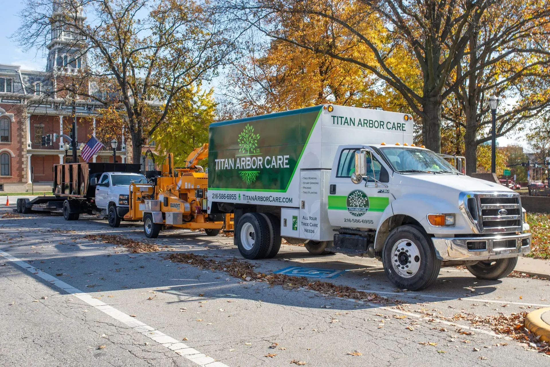 Tree service truck parked on a street with a wood chipper; fall foliage in the background.