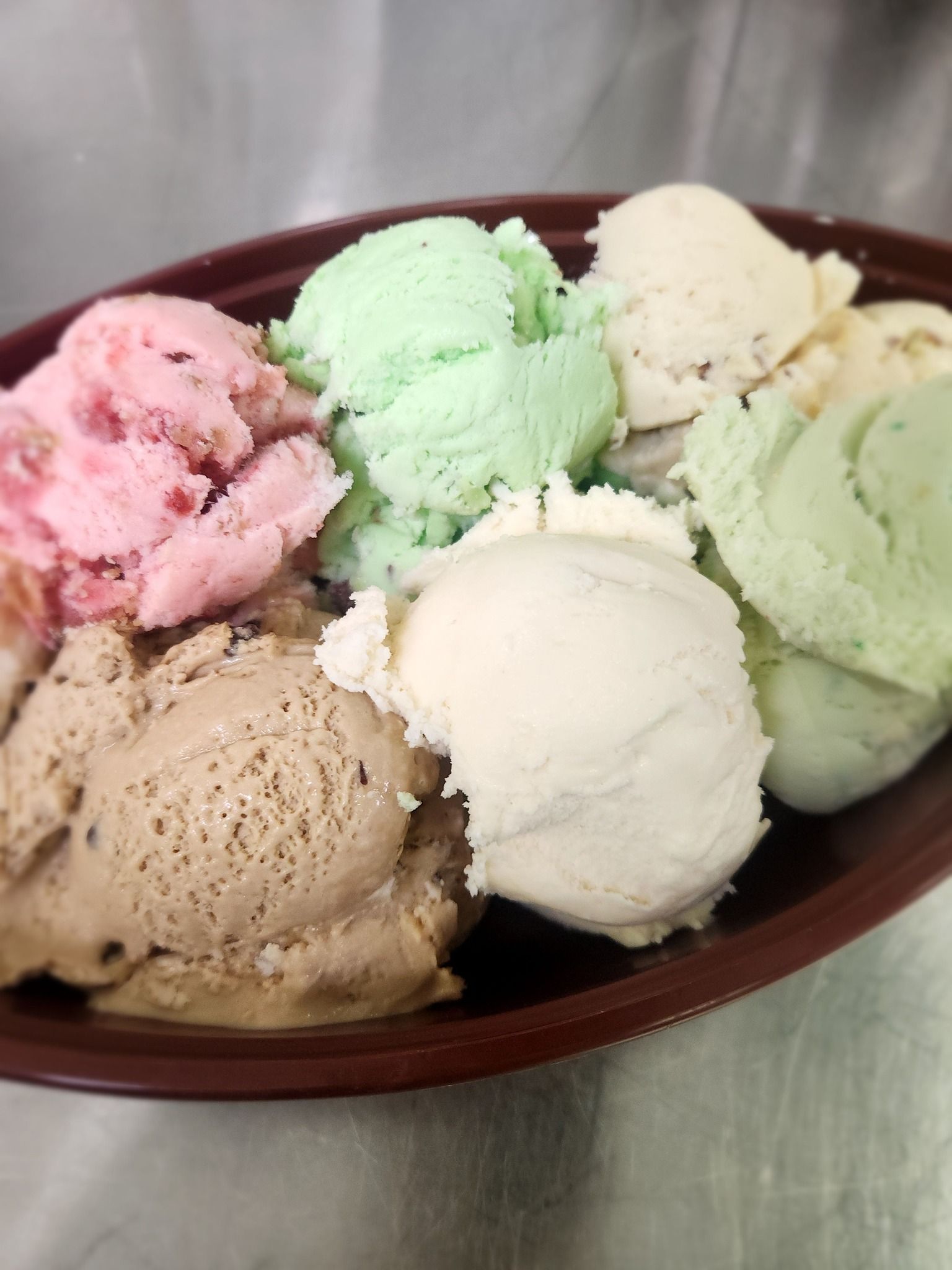 Bowl of assorted ice cream scoops in pink, green, beige, and brown on a table