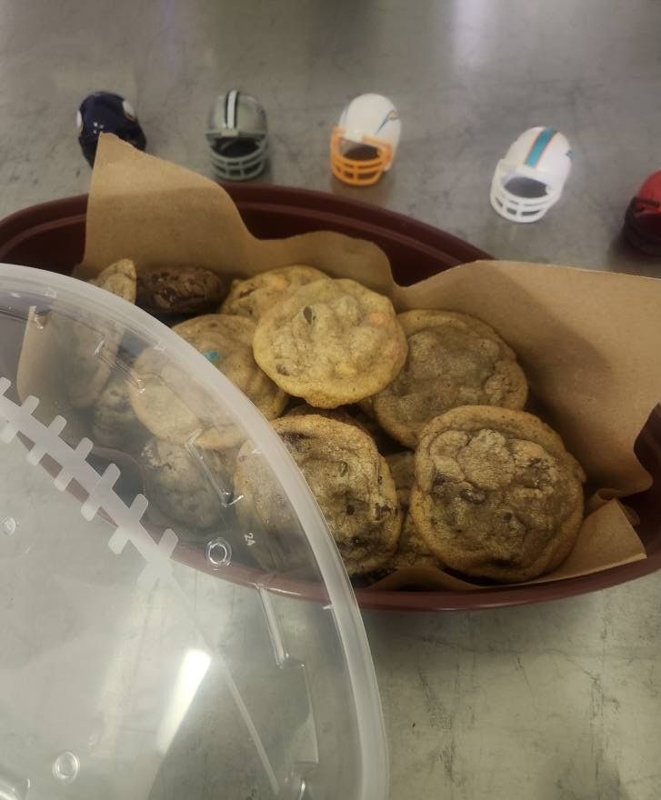 Tray of assorted cookies on brown paper in a plastic container, with tiny toy cars in the background.