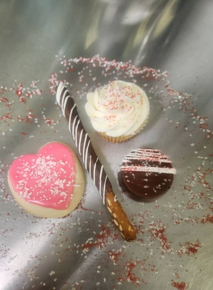 Three decorated heart-shaped chocolates and a striped chocolate stick on a silver tray with pink sugar sprinkles