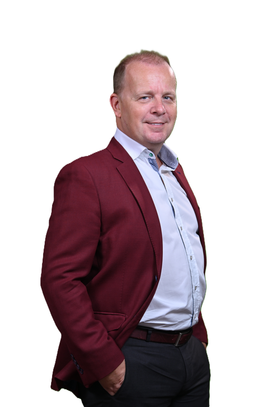 Man with short hair in a burgundy blazer and light blue shirt, smiling, hands in pockets.