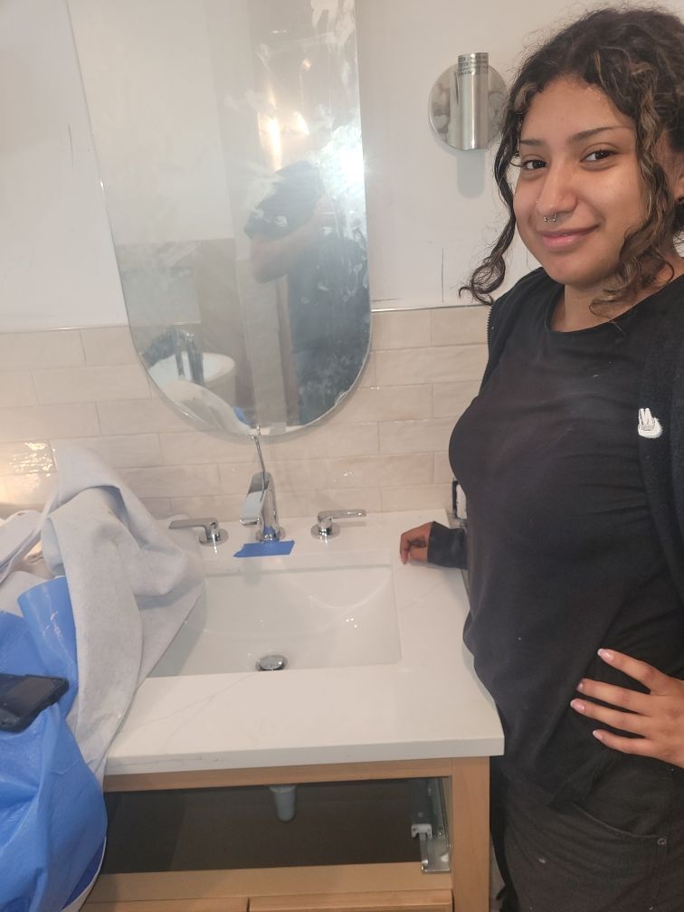 Woman in a black shirt smiling next to a new bathroom vanity. The vanity has a white countertop and chrome fixtures.