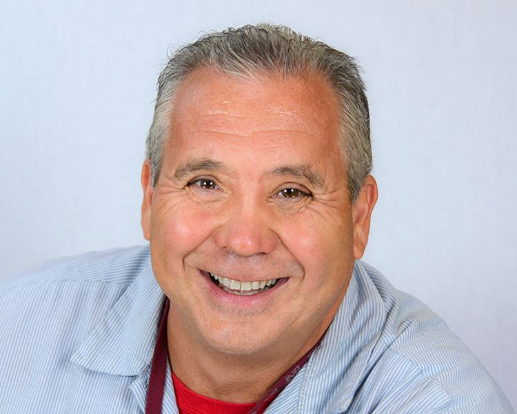 Owner of the Company - smiling middle-aged man with gray hair, wearing a red shirt and light blue striped button-up, against a white backdrop.