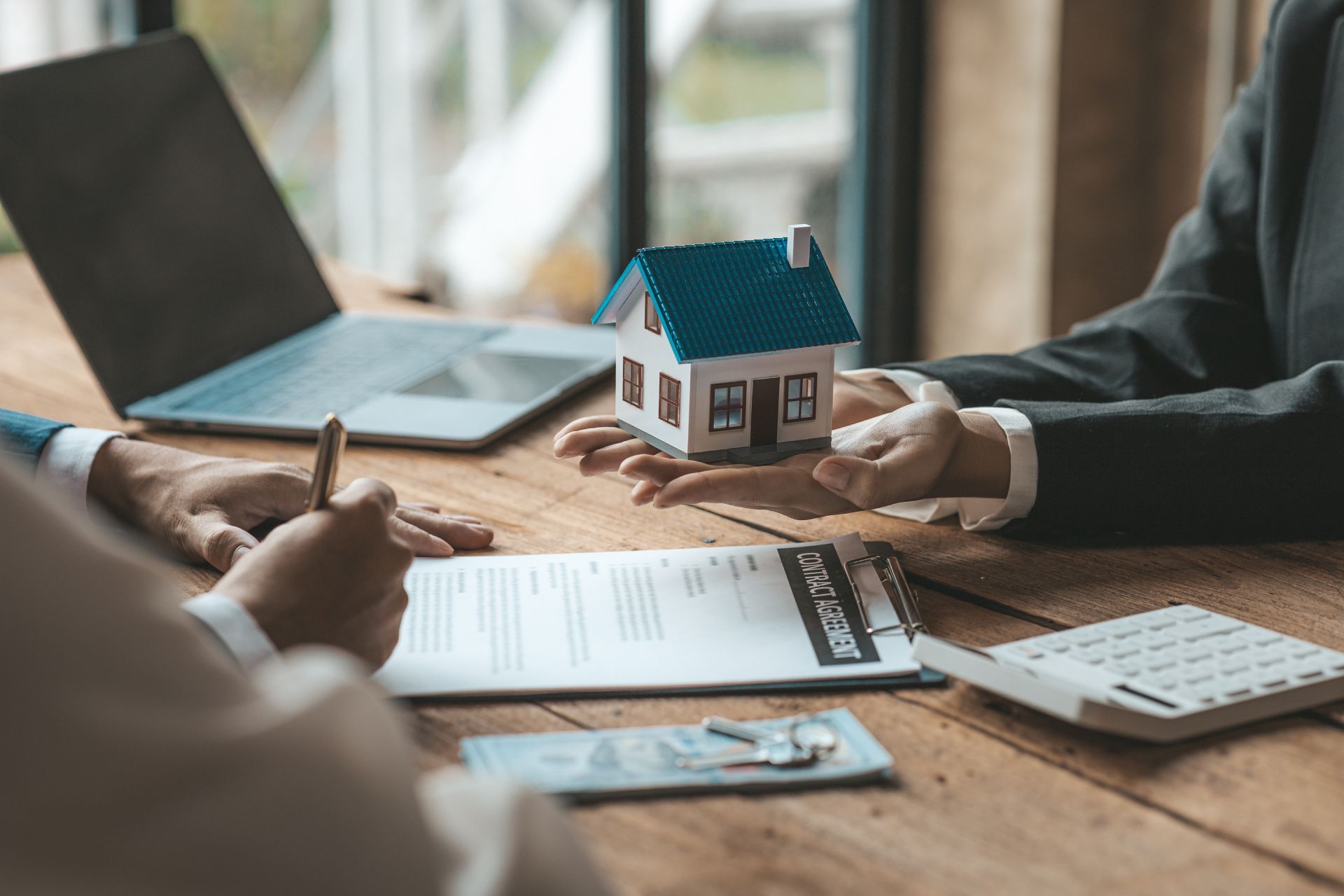 People reviewing house plans and a small model home at a table with laptop and calculator