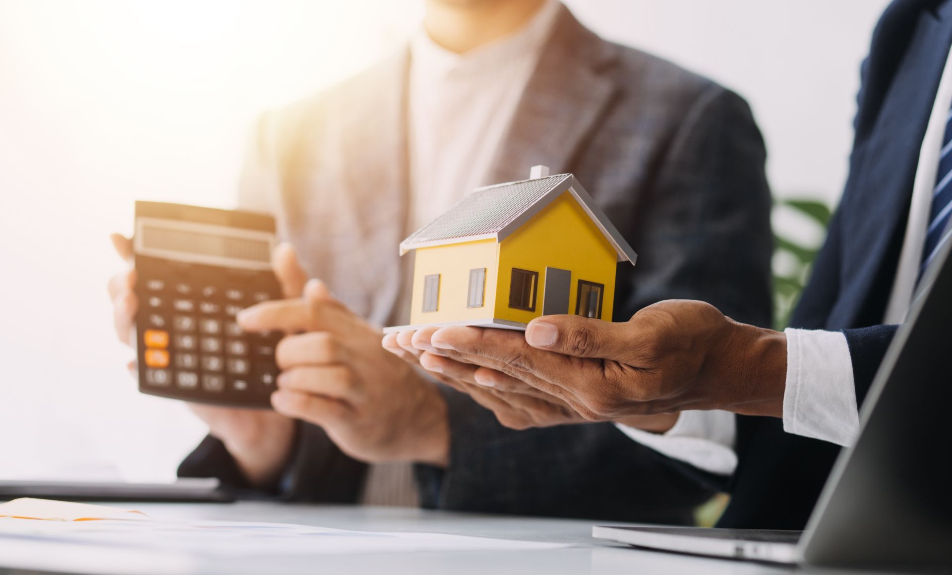 Business people holding a calculator and a small house model at a desk, discussing real estate investment