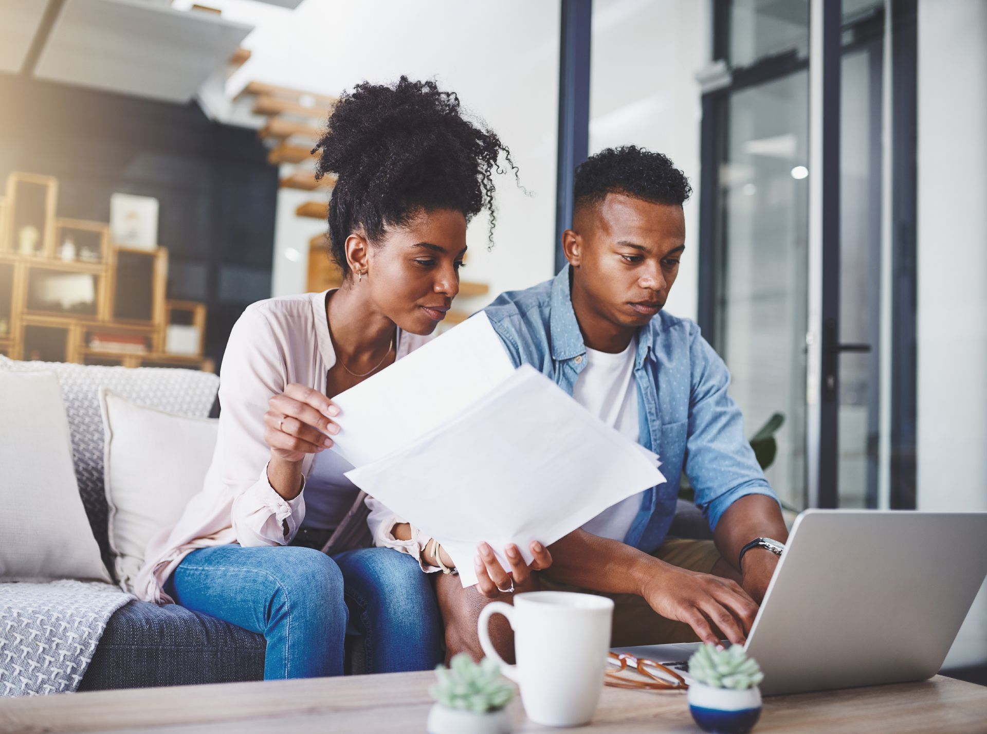 Two coworkers reviewing papers beside a laptop in a bright office lounge