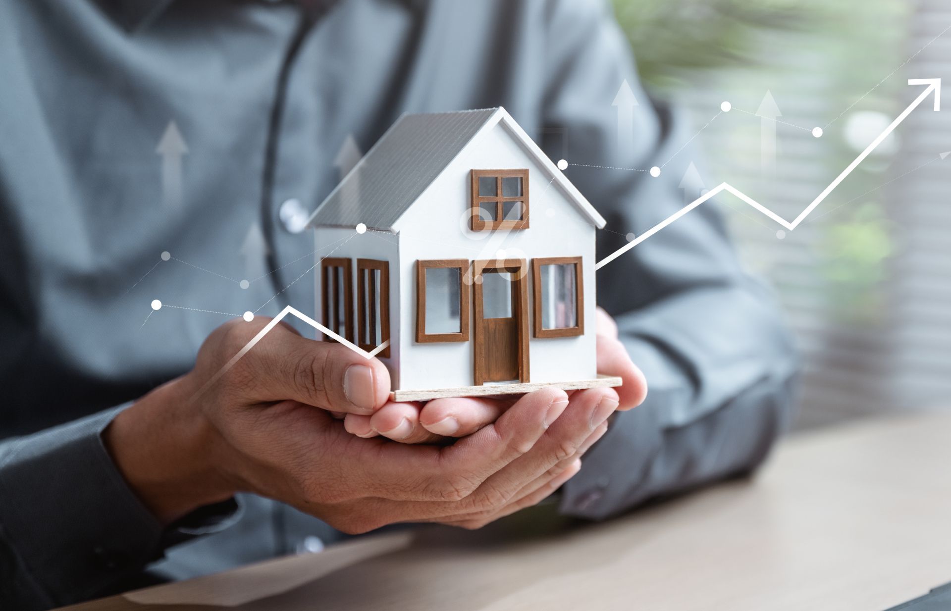 Hands cupping a small white house model, with faint rising arrow graphics in the background