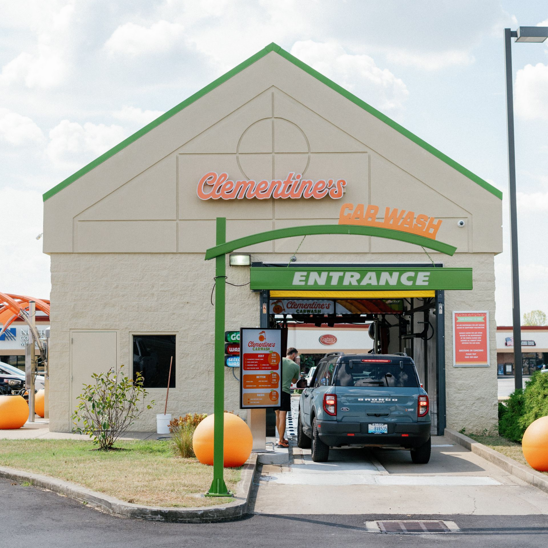 Convenience store drive-through entrance with a blue SUV and green awning, set in a beige building