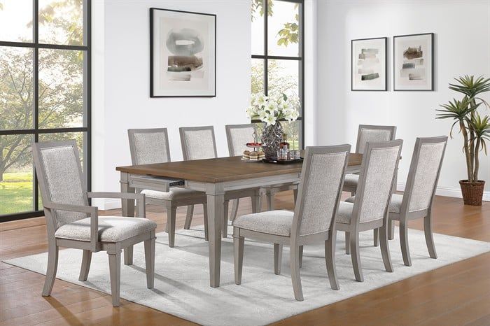 A wooden dining table with a dark top and light gray frame, surrounded by eight upholstered gray chairs in a bright room.
