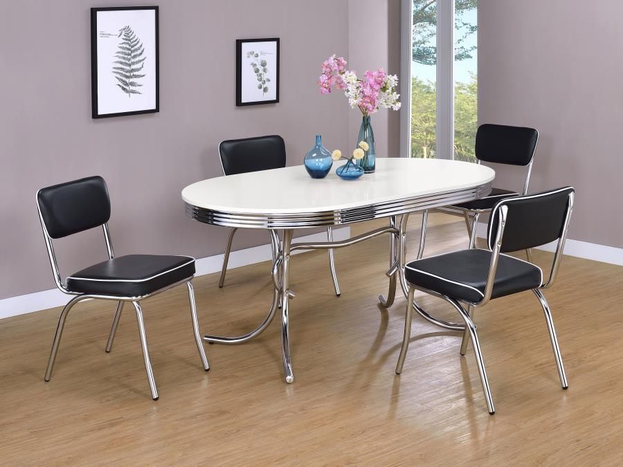 Retro dining set: oval white and chrome table with four black and chrome chairs. Flowers and art in room.