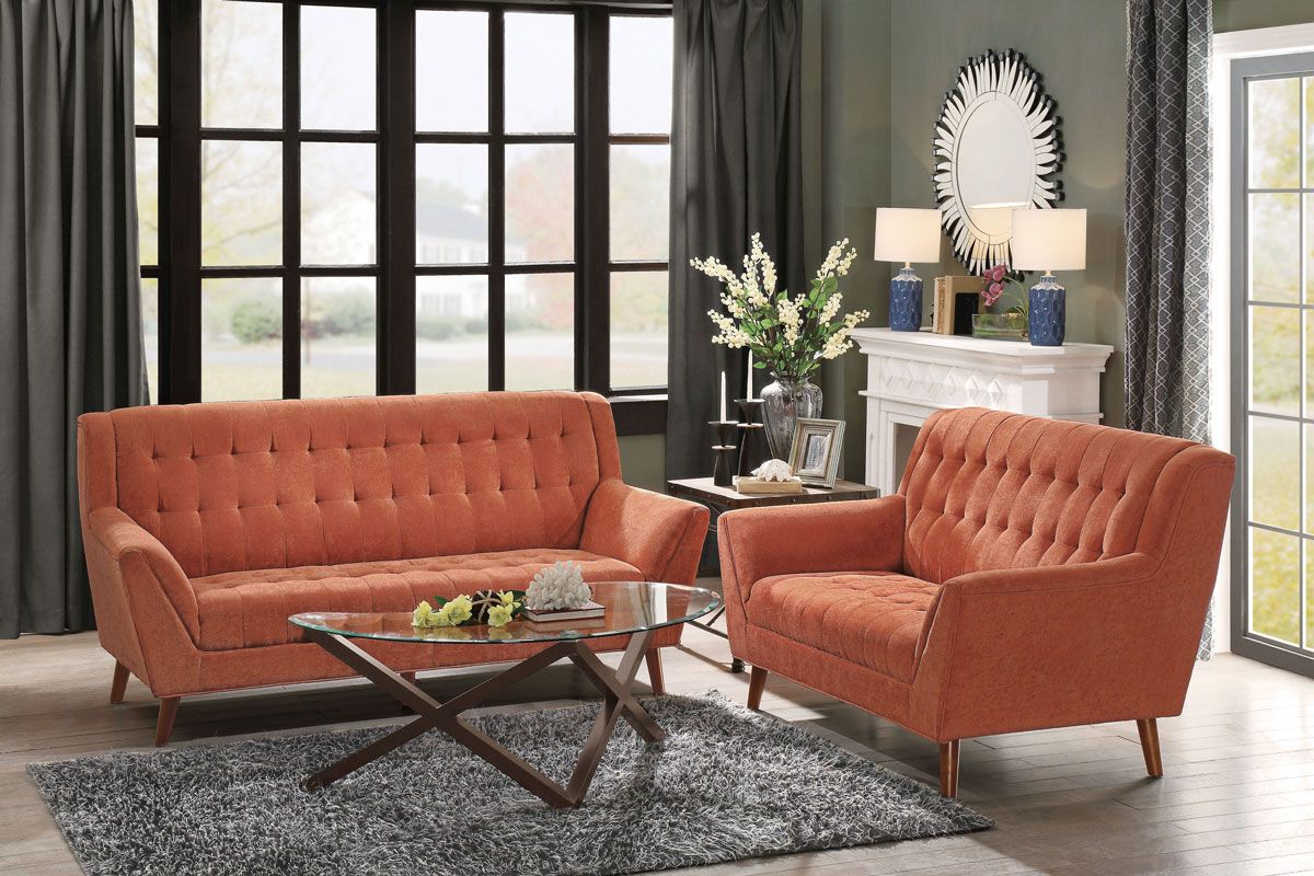 Orange tufted sofa and chair in a living room, with a glass coffee table and area rug.