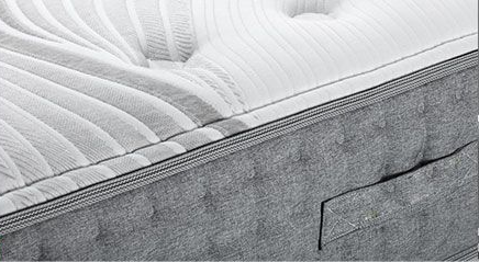 Close-up of a gray and white tufted mattress, showing stitching and a built-in handle.