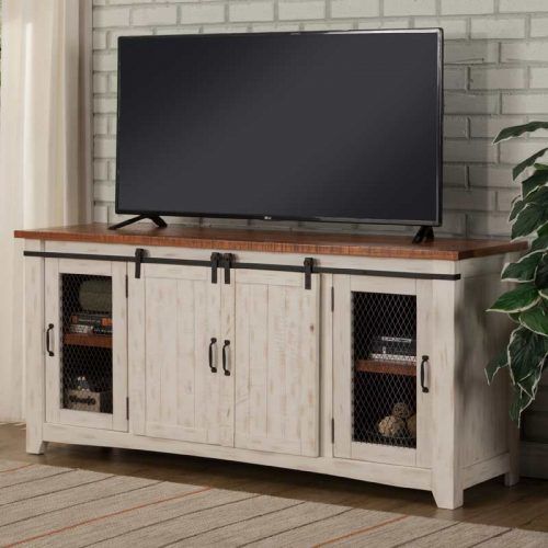 TV on a white-washed wood media console with sliding doors and a wire mesh accent against a brick wall.