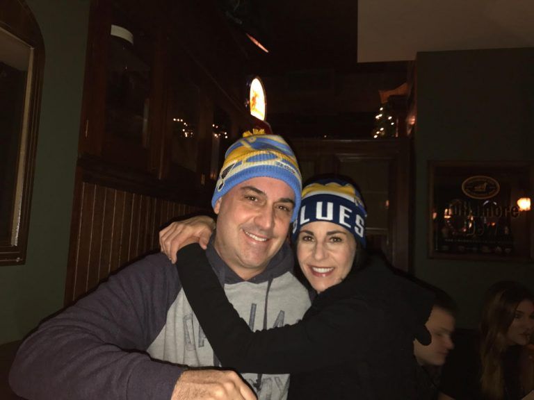 Two people wearing Blues hats in a dimly lit bar, hugging and smiling.