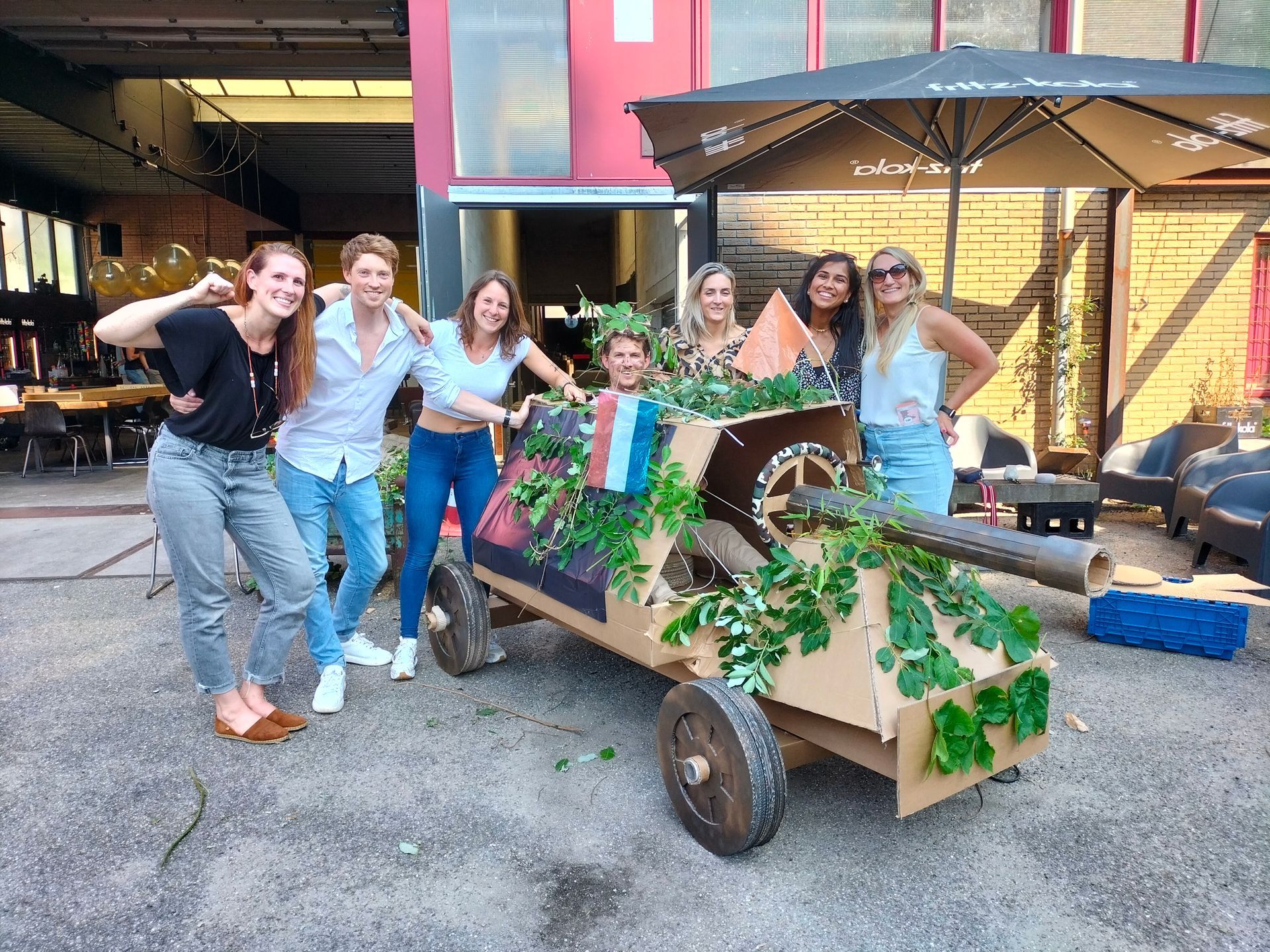 Een groep mensen poseert voor een foto voor een kartonnen auto.