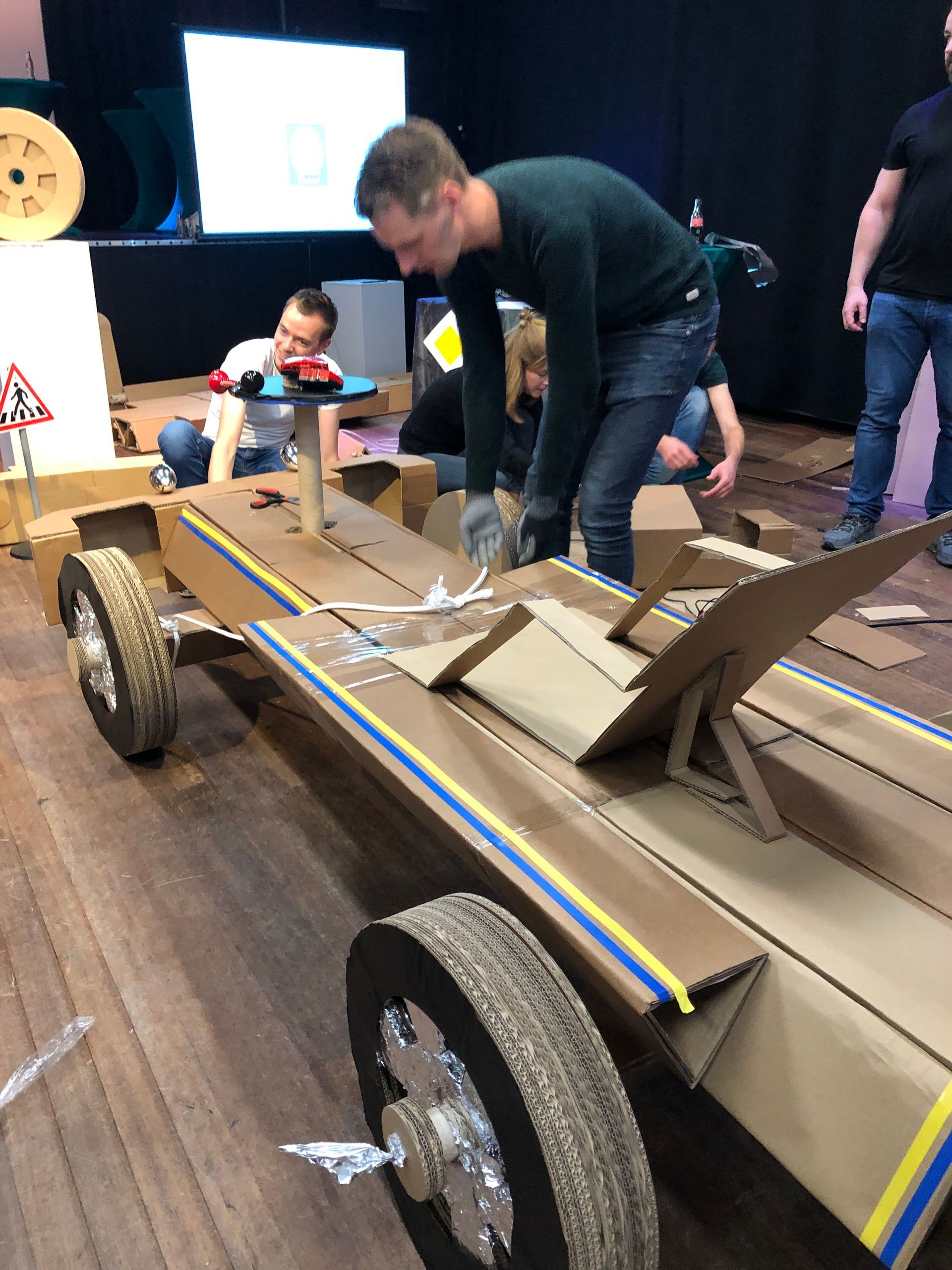 Een groep mensen werkt aan een kartonnen auto