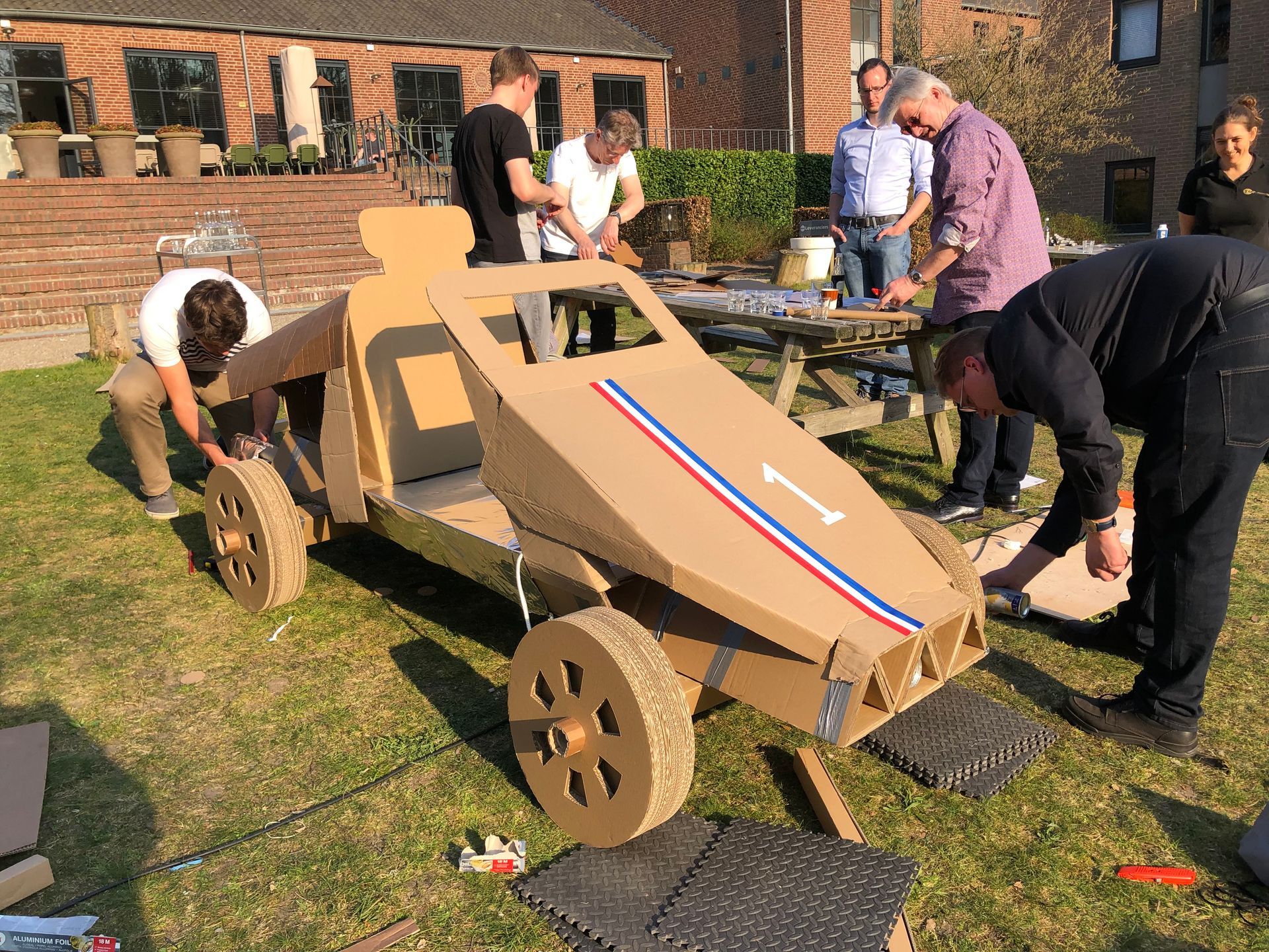 Een groep mensen werkt aan een kartonnen auto.