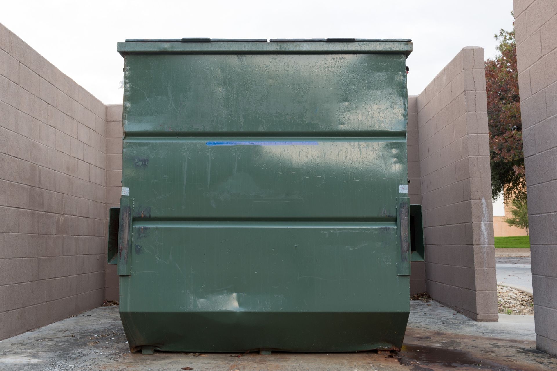A green dumpster is sitting in the middle of a brick building.