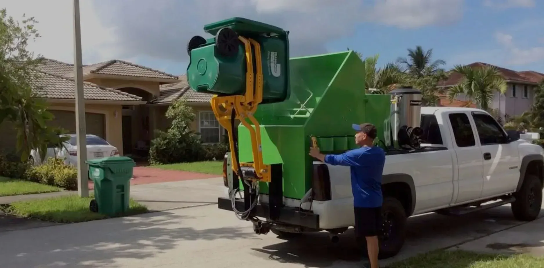 A man is loading a trash can into the back of a garbage truck.