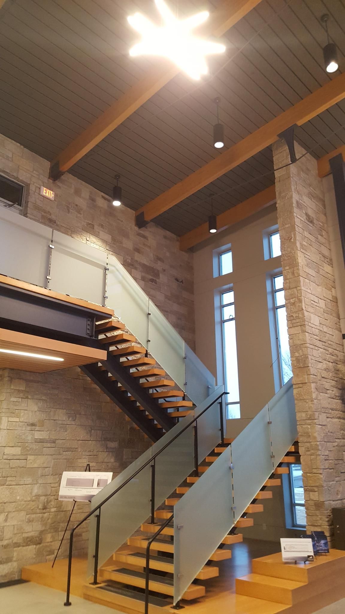 A staircase with a glass railing in a room with a brick wall.