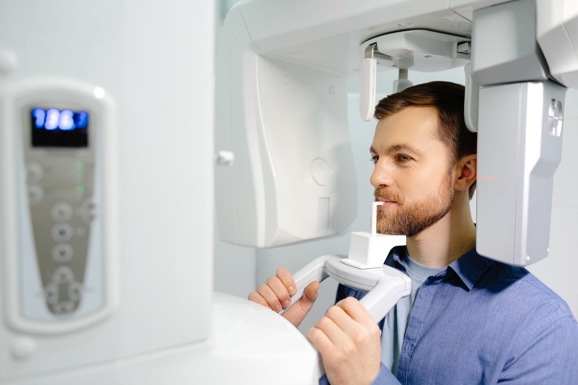Man undergoing a dental X-ray scan while holding a bite block in a clinic.