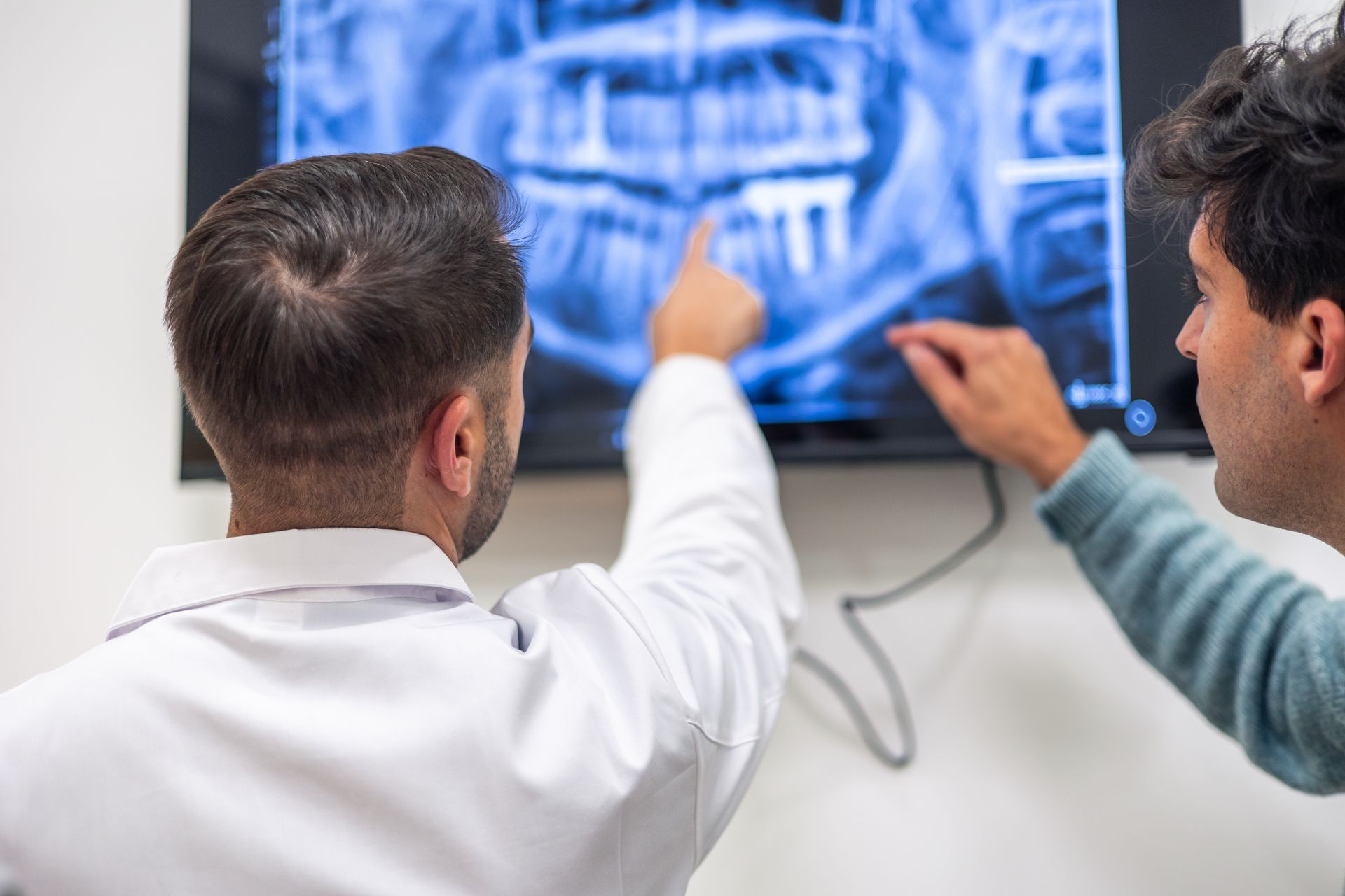 Two people pointing at a blue medical scan on a wall-mounted screen