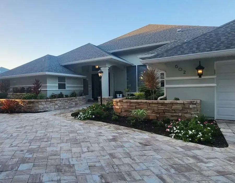 Modern suburban house with stone paver driveway, gray roof, and landscaped front entrance at dusk