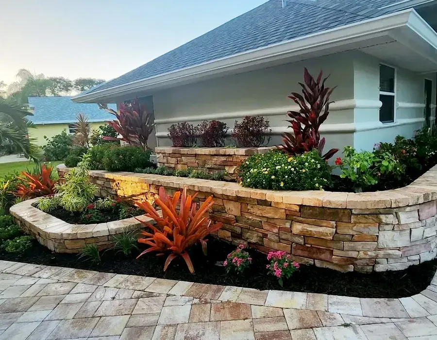 Modern house with stone planter beds, tropical landscaping, and a paved walkway