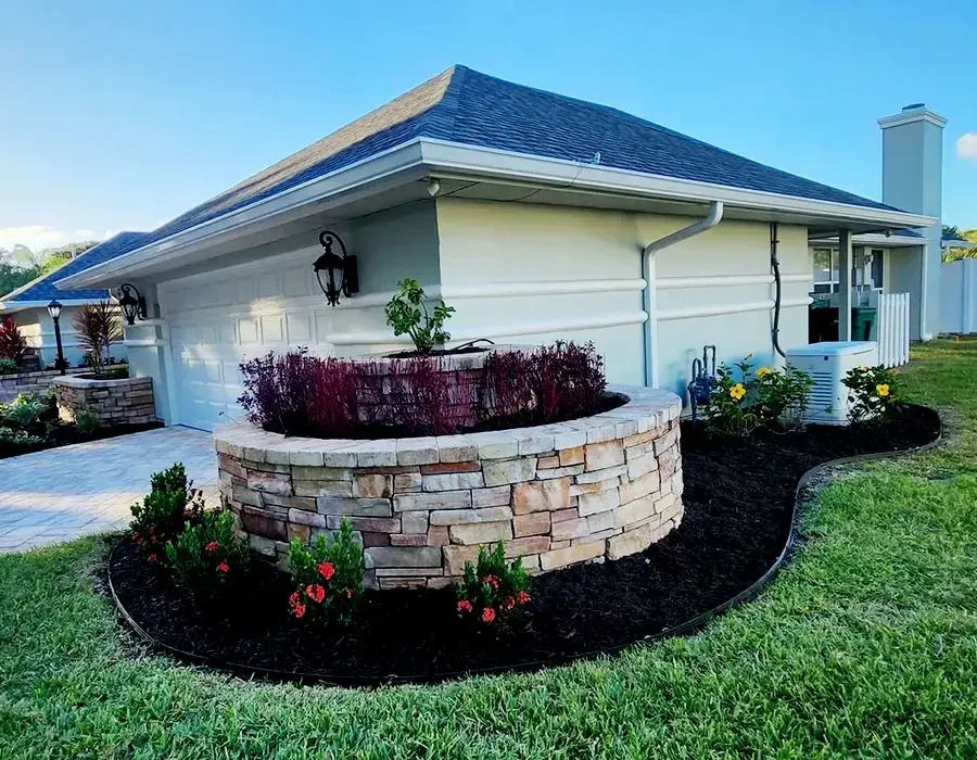 White house with blue roof and stone planter in landscaped yard