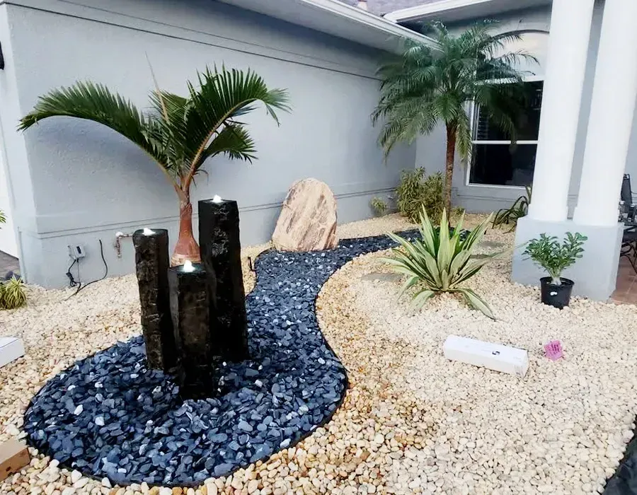 Modern front yard with black stone feature, palm plants, and white gravel landscaping