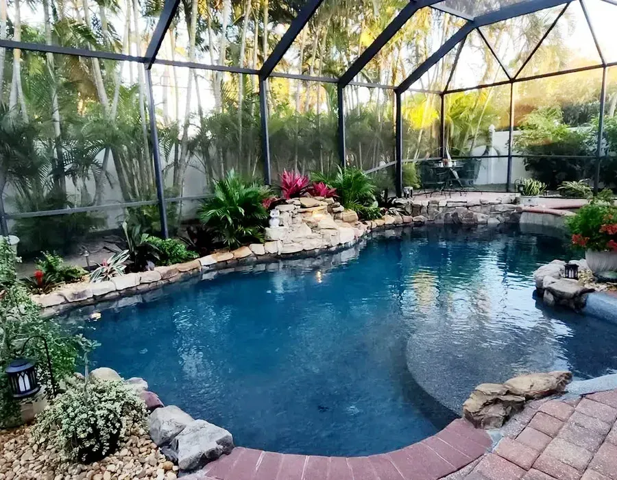 Indoor tropical pool surrounded by lush plants, rocks, and screened enclosure