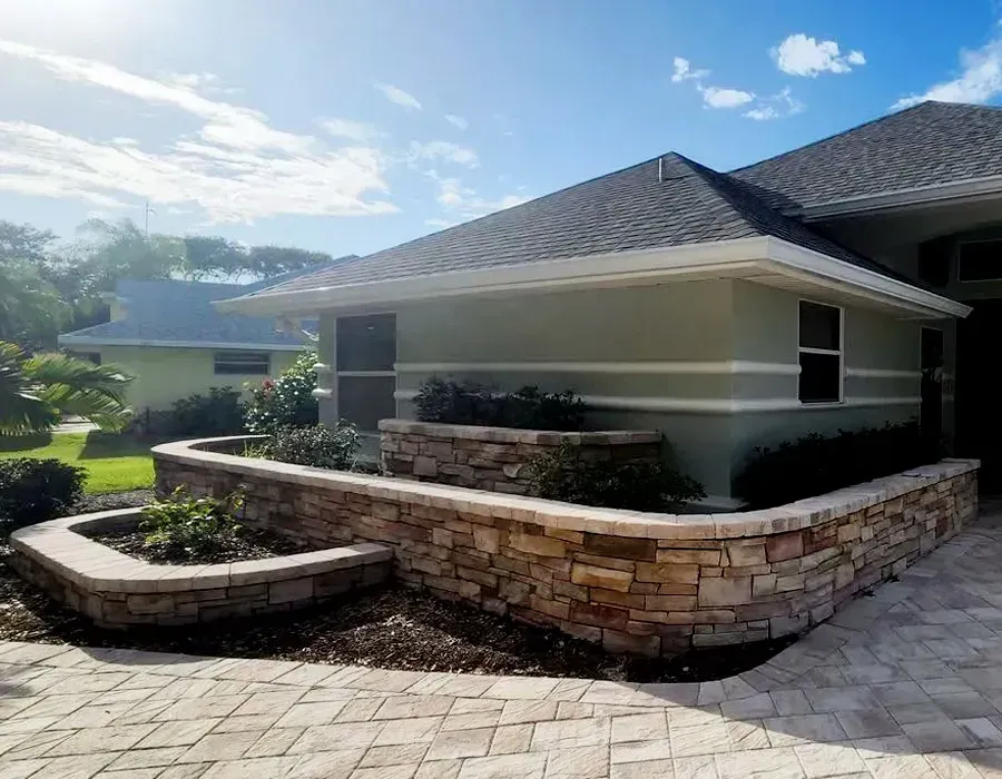 Stone retaining wall and curved walkway around a modern house with gray roof under a bright blue sky