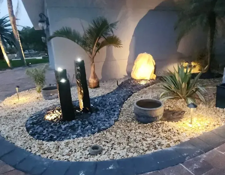 Landscape lighting in a rock garden with palm plants and a glowing decorative stone at dusk