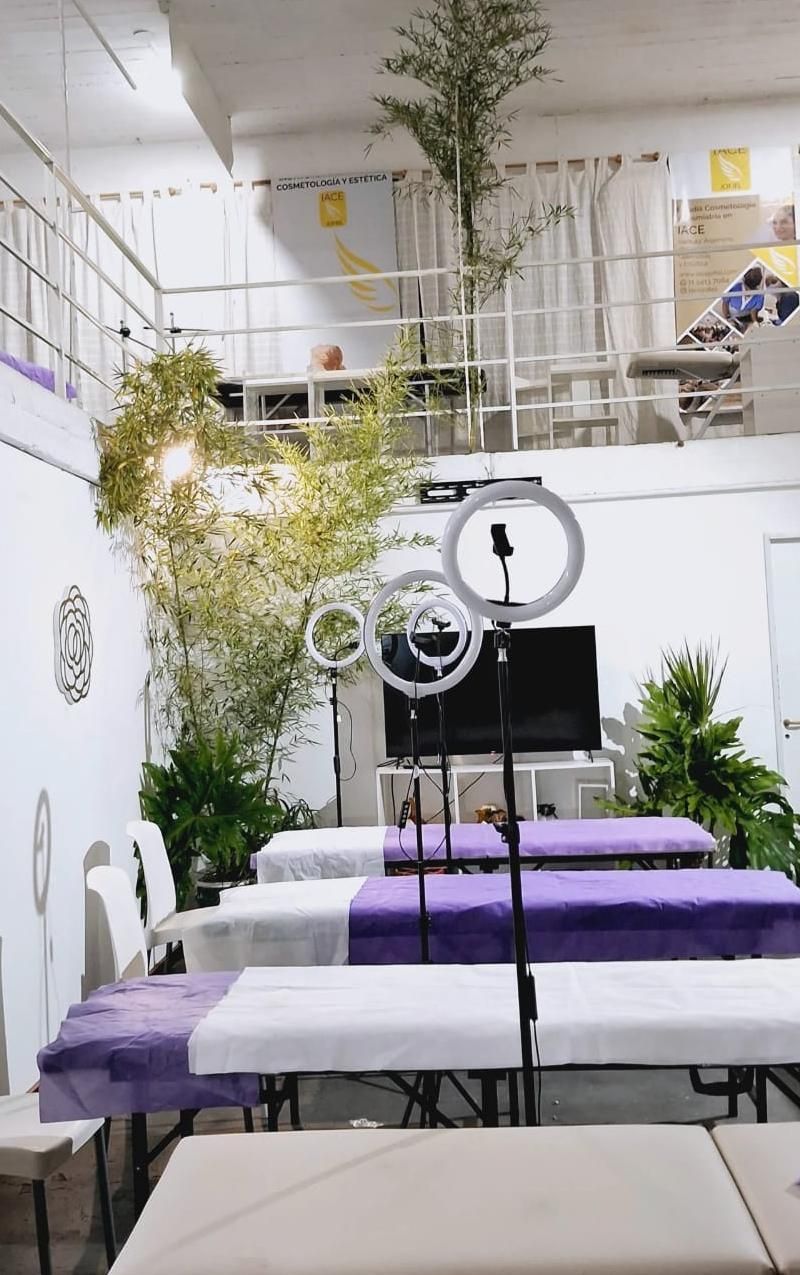 Estudio blanco luminoso con aro de luz, camillas de masaje moradas, plantas y zona de estar tipo loft.