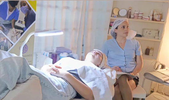 Dos personas en una luminosa sala médica; una está recostada en una silla mientras la otra está sentada a su lado con uniforme quirúrgico.