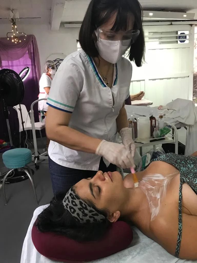 Un profesional sanitario enmascarado atiende a una clienta tumbada en una camilla de spa durante un tratamiento facial.
