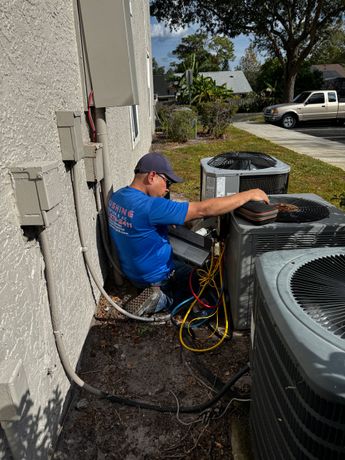 HVAC technician in blue shirt and cap working on an outdoor air conditioning unit.